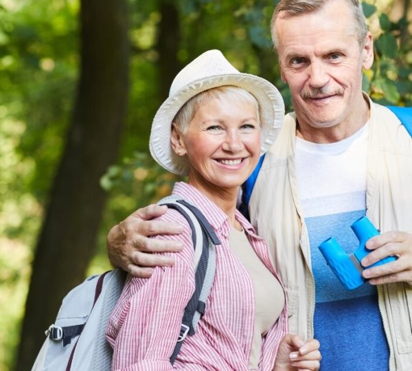 Seniors' couple smiling, hiking, with binoculars and backpack