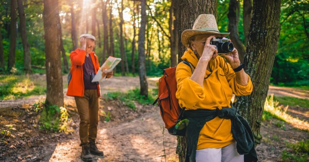 Middle aged couple hiking in a forest with binoculars and map